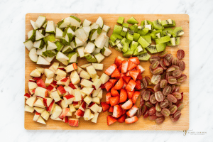 Chopped fruit for salad on a wooden cutting board.