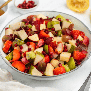 a white bowl filled with fruit salad for thanksgiving, featuring apples, pears, grapes, strawberries, and pumpkin pie spice