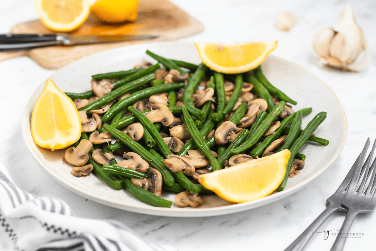 a large white plate filled with sauteed green beans and mushrooms, on a table, viewed from the side. 