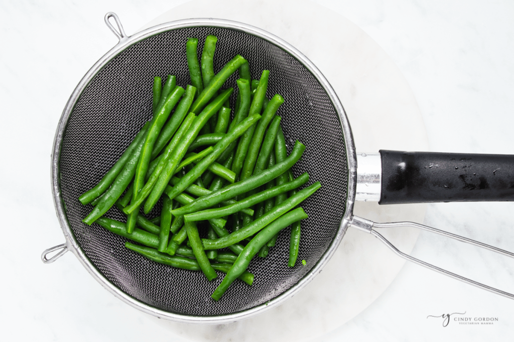 blanched green beans in a mesh strainer, viewed from above.