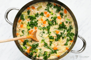 Creamy soup with kale and carrots in a stock pot. A spoon is stirring.