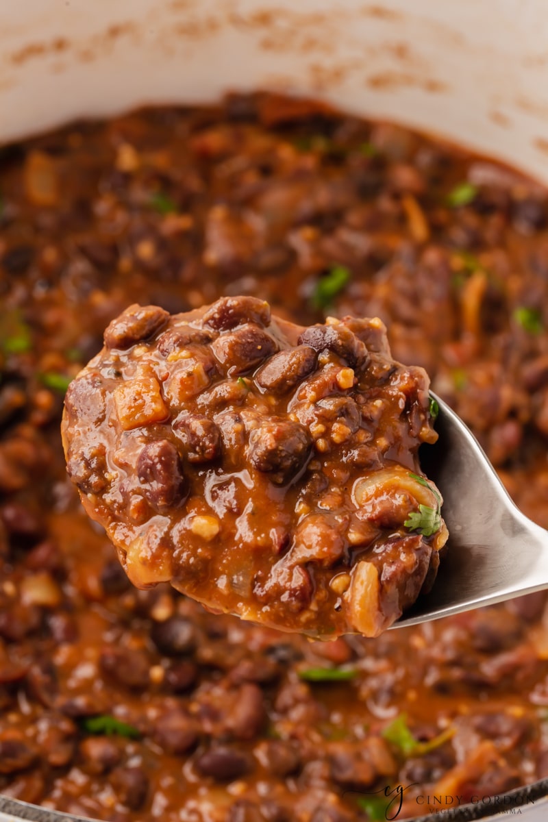 seasoned chipotle black beans in a pot. A spoon is holding some up to show the thick saucy texture.