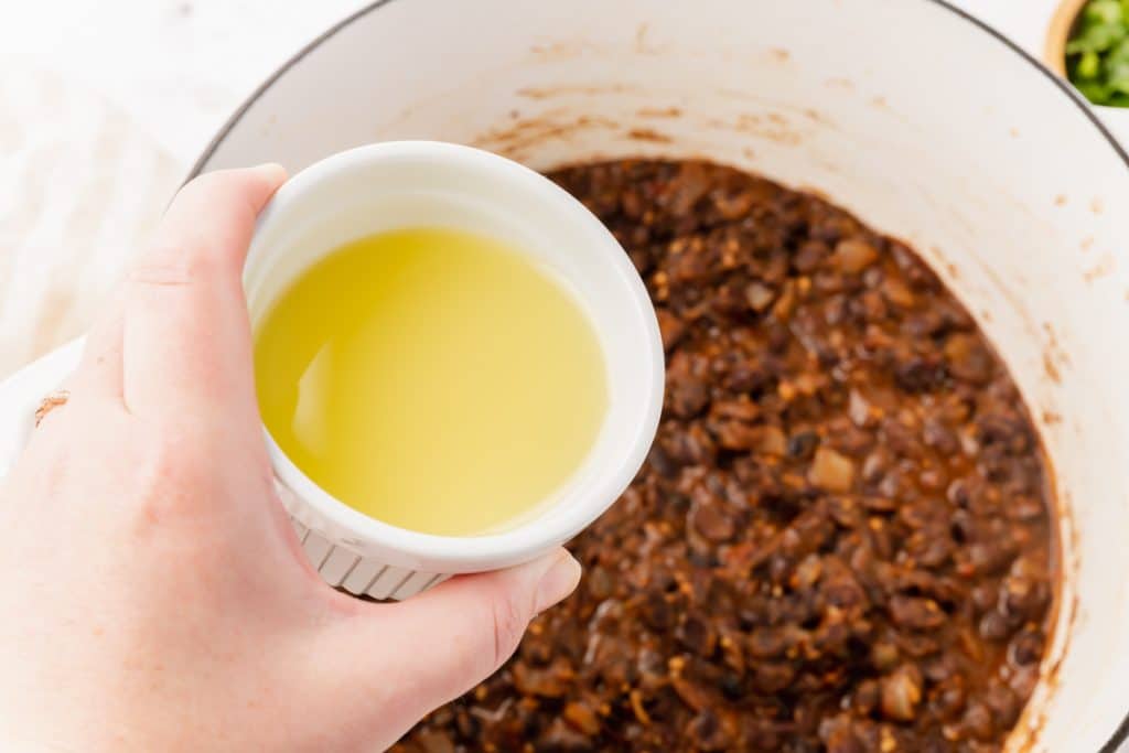 a hand adding a small cup of lime juice to a pot of seasoned chipotle black beans