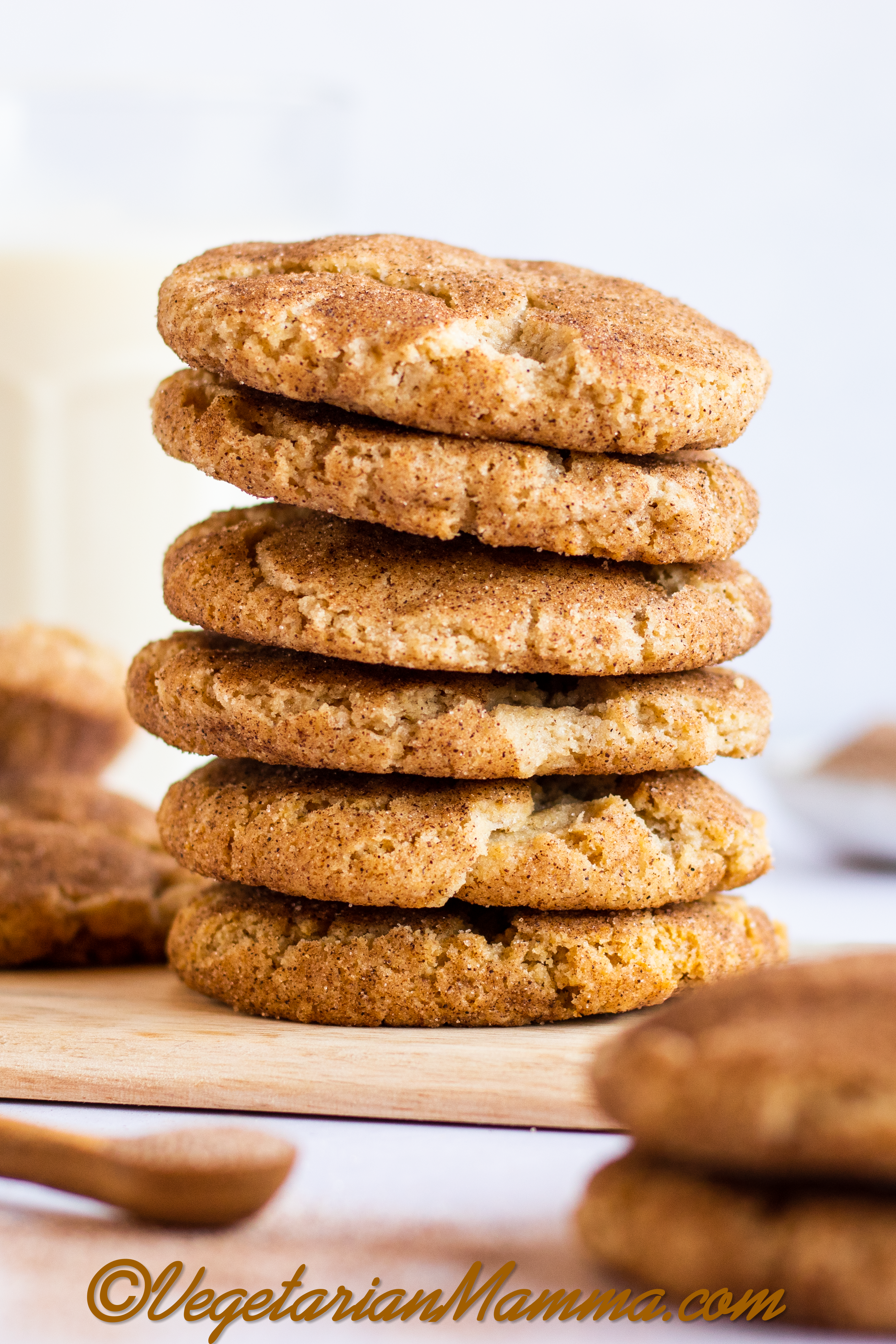 A stack of 6 snickerdoodle cookies on a wooden cutting board surrounded by more cookies