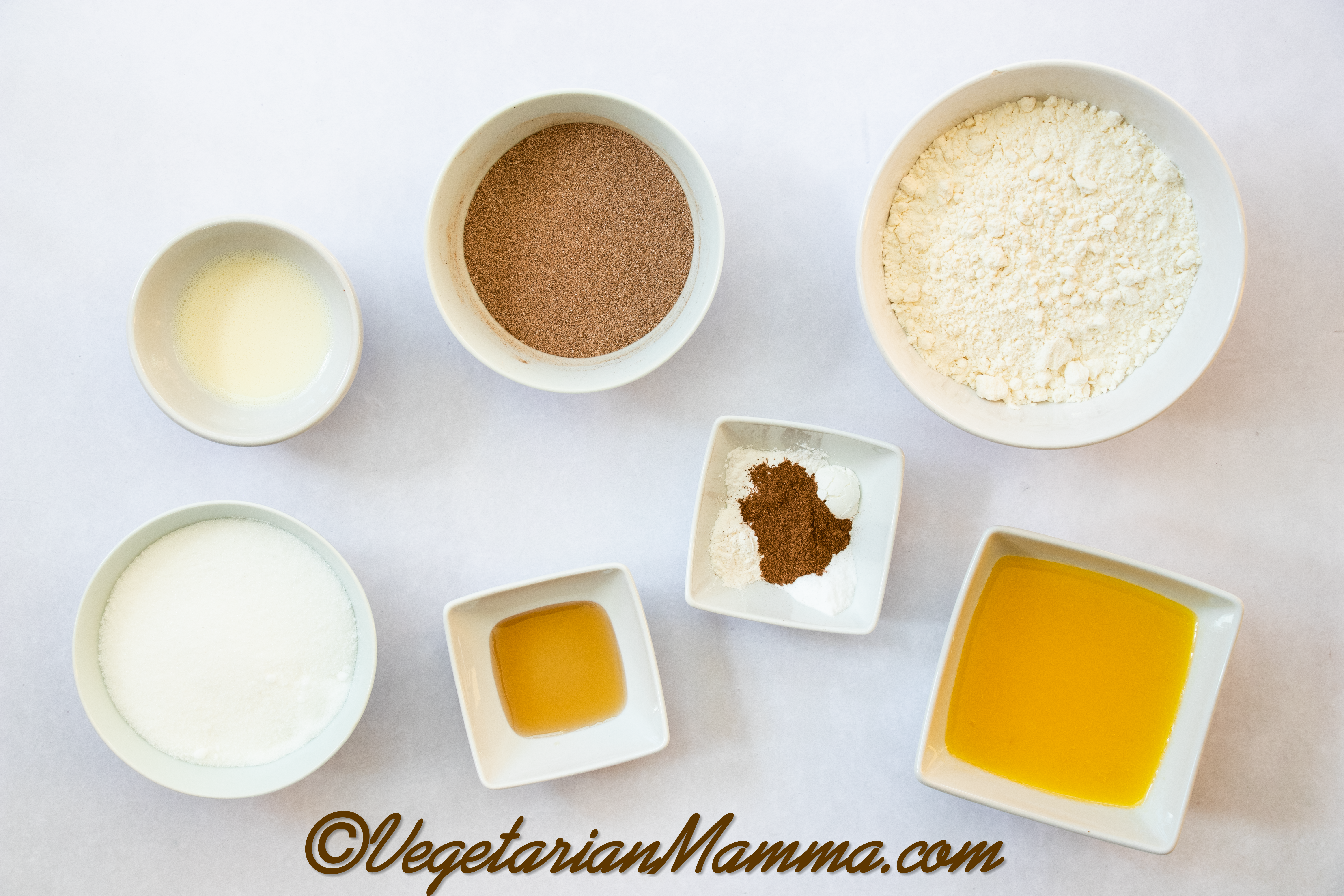 Bowls of sugar, almond milk, cinnamon, sugar, vanilla extract, almond flour, xanthan gum, cream of tartar, and vegan butter
