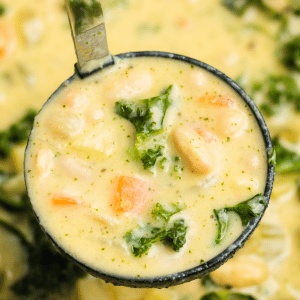 a ladle filled with white bean and kale soup, held over a pot of soup.