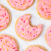 A set of pink frosted cookies with the middle one has a bite taken out.