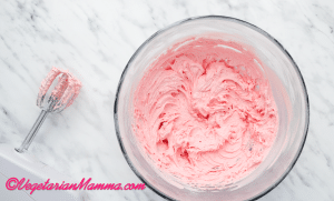 Once all of the powdered sugar has been added and the mixture is smooth and fluffy, add the pink food coloring a few drops at a time until your desired color is reached.
