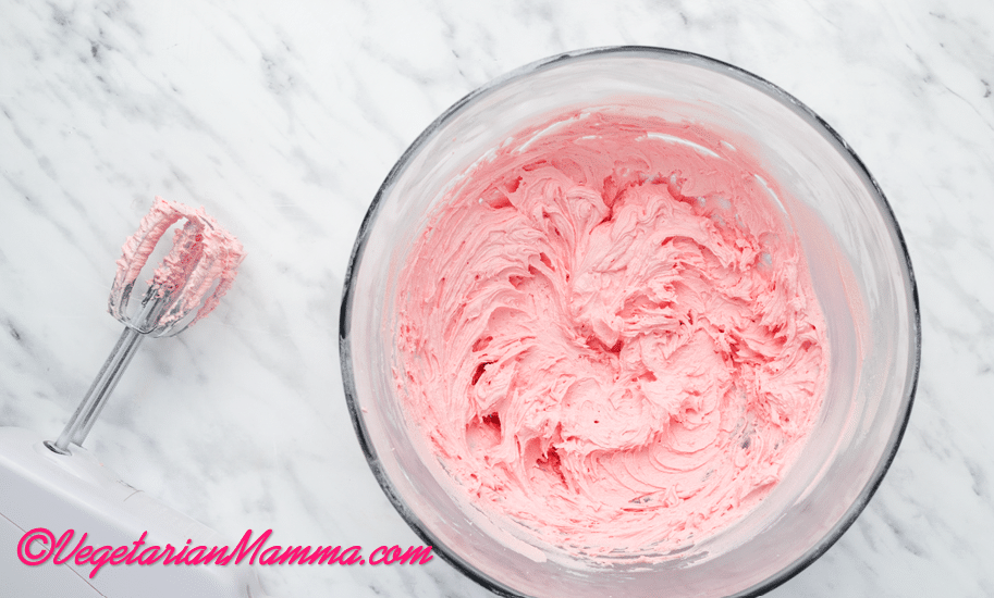Once all of the powdered sugar has been added and the mixture is smooth and fluffy, add the pink food coloring a few drops at a time until your desired color is reached.
