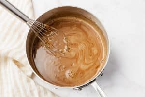 A whisk stirring vegan hot chocolate in a saucepan.