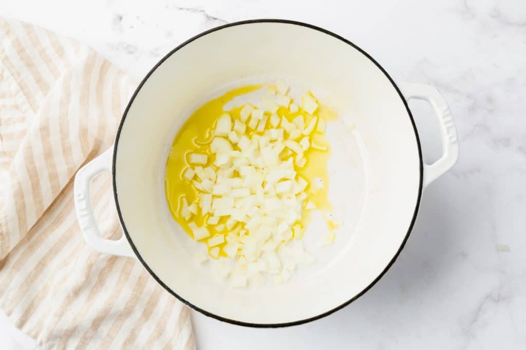 olive oil and diced onions in a white dutch oven.