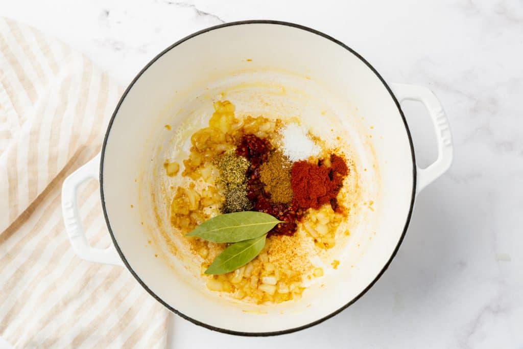 spices added to sauteed onions in a white soup pot.