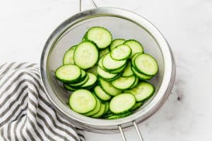 a mesh sieve filled with thinly sliced cucumbers.