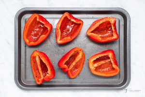 six red pepper halves on a sheet pan, to be roasted.