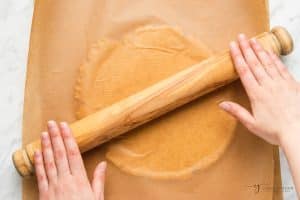 hands using a rolling pin to roll dough between two pieces of parchment paper