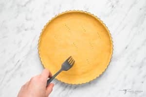 a fork making holes to dock pie crust in a pan.