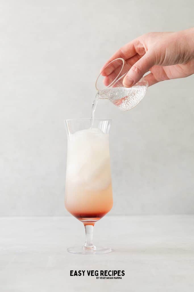 bubbly clear liquid being poured into glass with ice and red liquid