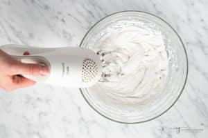 coconut cream being whipped with a mixer in a glass bowl.