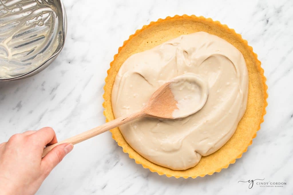 coconut filling being spread into a pie crust with a wooden spoon.