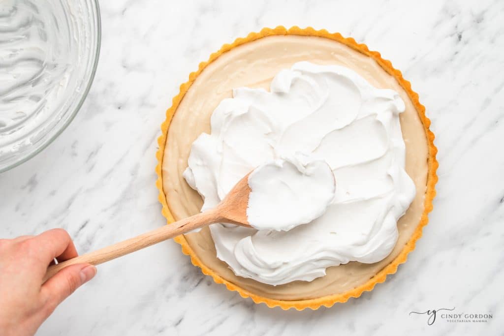 a wooden spoon spreading coconut cream over pie filling.