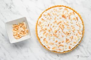toasted coconut being sprinkled on top of a vegan coconut cream pie.