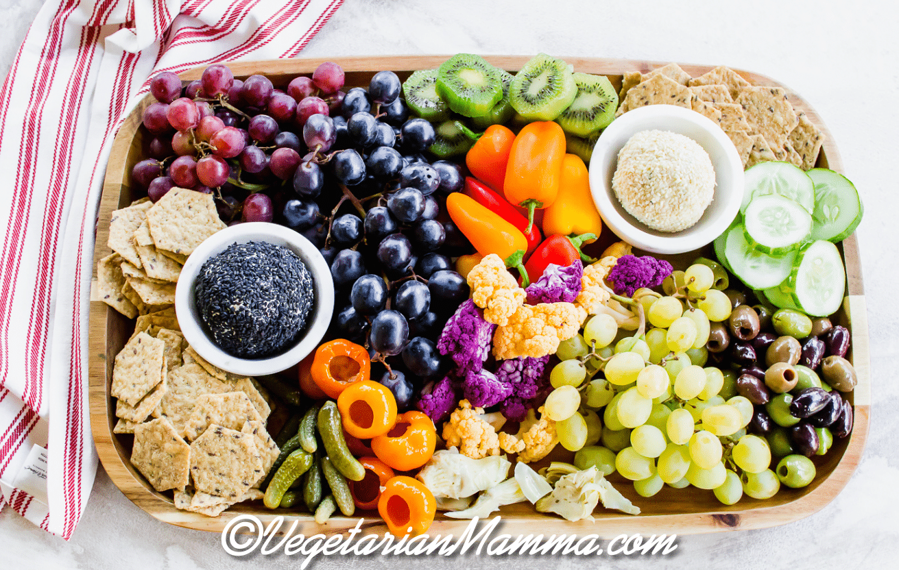 a wooden board filled with Vegetarian Charcuterie items like seed crackers, grapes, peppers, and cucumbers.