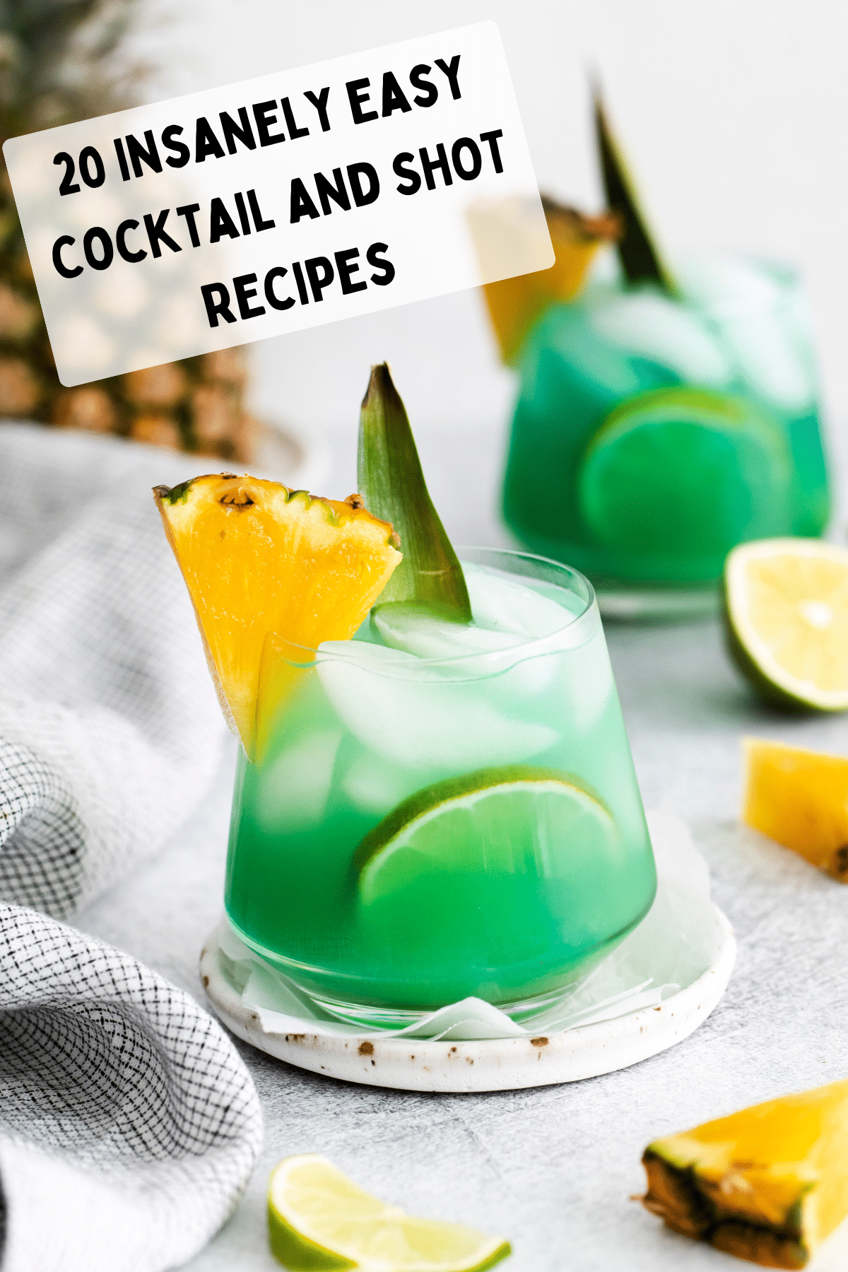 text overlay: 20 insanely easy cocktail recipes. A clear glass with ice cubes and green/blue liquid inside. A pineapple chunk on top left of class and limes around the glass on table