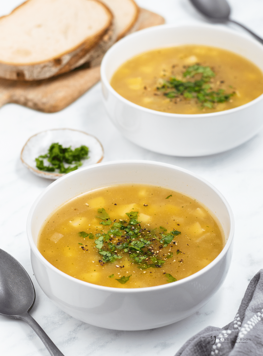 two bowls of simple 3 ingredient potato soup on a table next to a stack of sliced bread. 