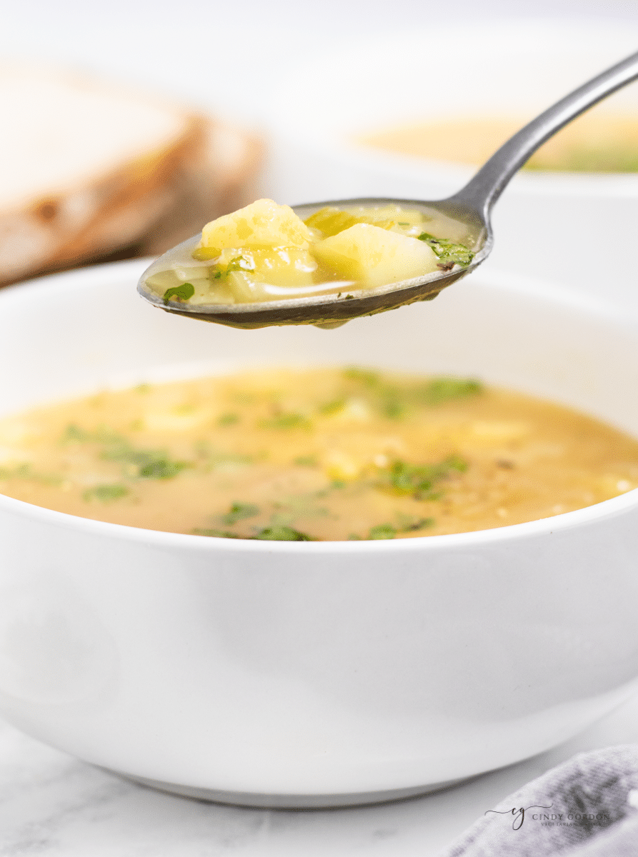 closeup shot of a bowl of simple potato soup. A spoon is holding up a serving. 