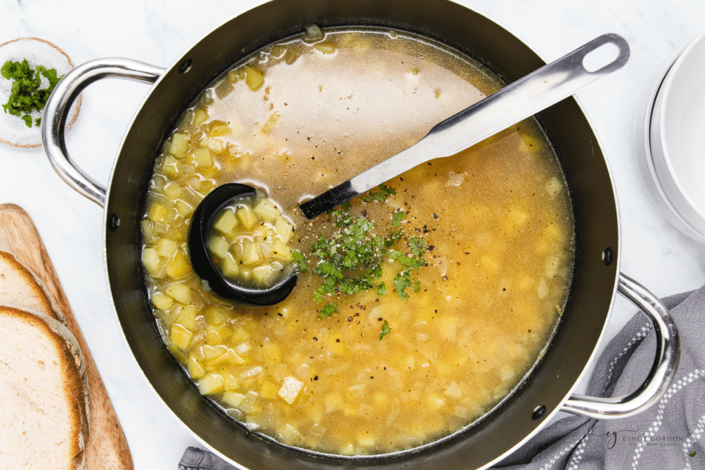 a pot of potato soup garnished with parsley. A ladle is in the pot.