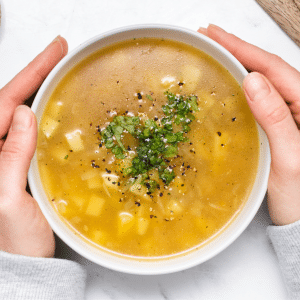 A bowl of potato soup held by two hands, viewed from overhead.