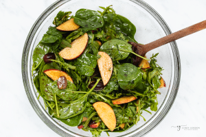 Apple pecan salad tossed with arugula and baby spinach in a mixing bowl.