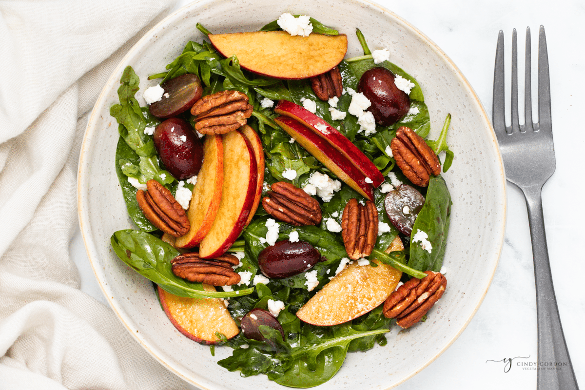 a green salad with apples, grapes, pecans, and feta cheese, on a plate, next to a fork. 