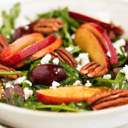 closeup of a salad of greens topped with apples, grapes, pecans and feta