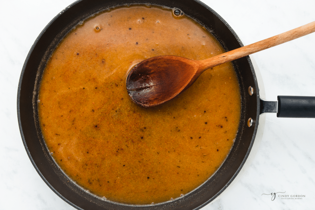 A skillet with broth and seasonings, stirred with a wooden spoon.