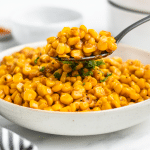 A large white serving bowl filled with cajun fried corn. A spoon is lifting up a serving.