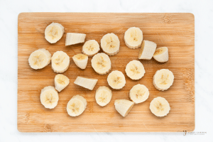 a wooden cutting board holding thickly sliced bananas.