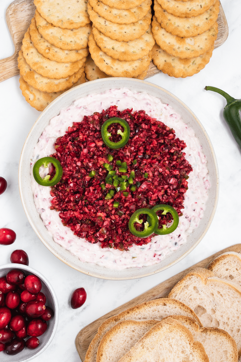 a bowl of cranberry jalapeno dip viewed from above, served with crackers and bread. 