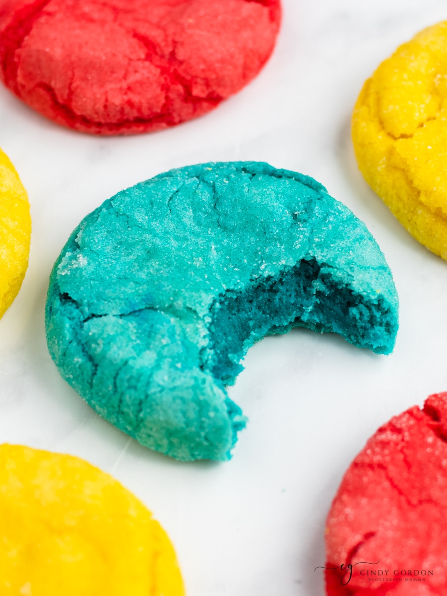 colorful mexican sugar cookies. One blue one has a bite taken, showing the soft inside. 
