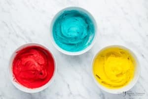 three bowls of cooking dough, one red, one blue, and one yellow.