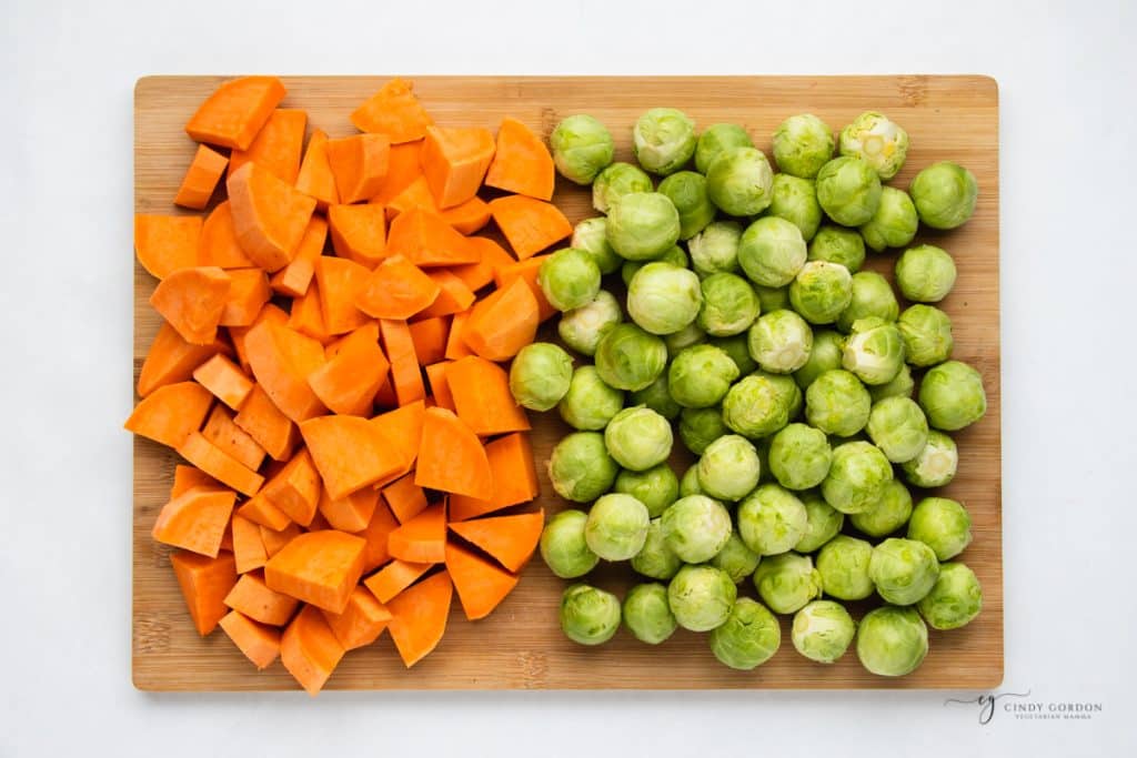 diced sweet potatoes and trimmed brussels sprouts on a wooden cutting board.