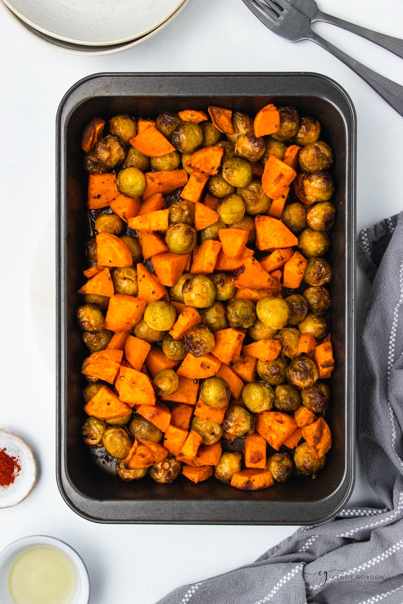 a metal casserole pan with browned, roasted brussel sprouts and sweet potatoes in it. 