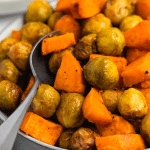 a bowl of roasted sweet potatoes and brussel sprouts with a serving spoon in it.