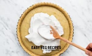a wooden spoon spreading whipped cream over a vegan pie.