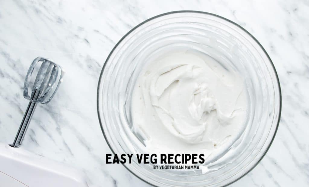 whipped coconut cream in a glass bowl next to a mixer.