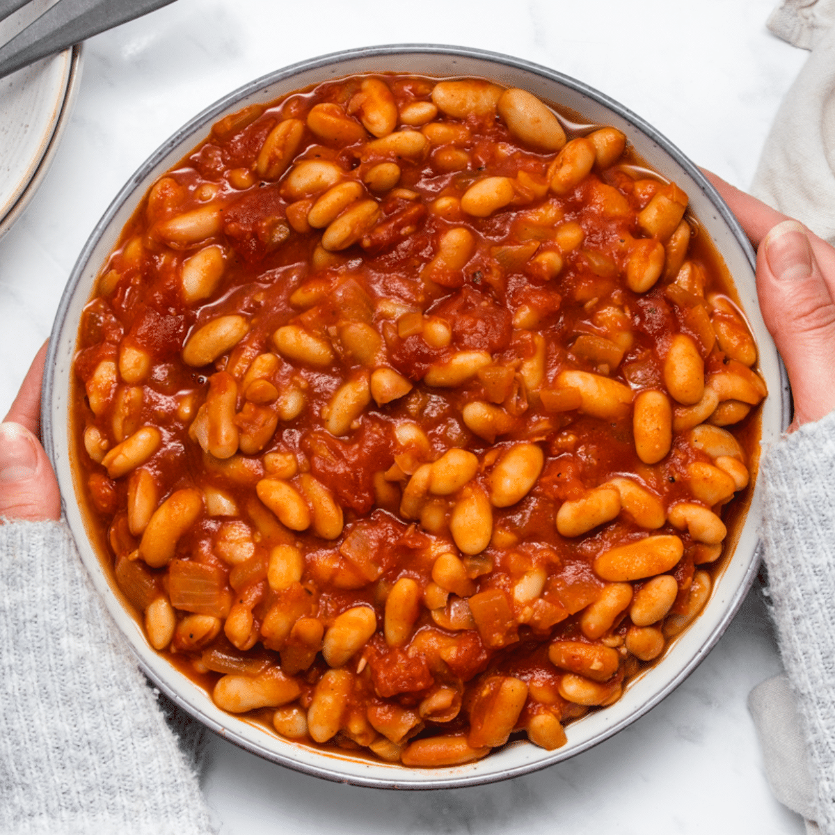 a woman holding a large bowl of vegan baked beans.