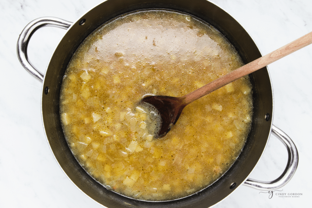 potato soup cooking in a pot with a wooden spoon in it.