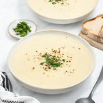 a rustic bowl filled with creamy potato soup. Behind the soup is sliced bread and another bowl of soup.