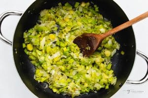 leeks, onion, and garlic, in a frying pan with a wooden spoon.