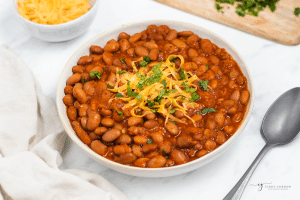 a bowl filled to the top with seasoned ranch style beans. They are topped with shredded cheese and herbs.